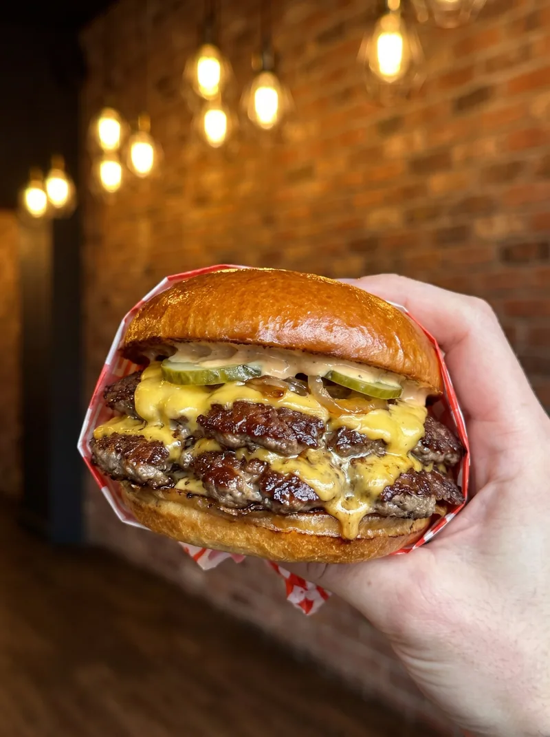A double cheeseburger held in one hand